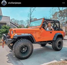 a woman sitting in the driver's seat of an orange jeep parked next to a house