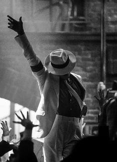 a man in a suit and hat on stage with his arms up to the crowd