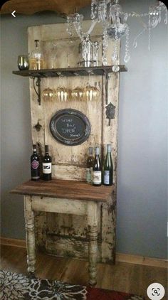 an old wooden table with bottles and glasses on it, next to a chandelier