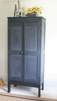 a black armoire sitting next to a wall with pictures on it and a vase filled with flowers