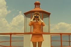 a woman in an orange dress is looking through binoculars at the ocean while standing on a boat