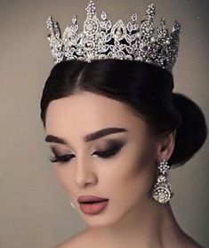 a woman wearing a tiara and makeup looks down at her left shoulder as she poses for the camera