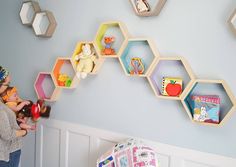 a woman holding a baby in her hands while standing next to a wall with hexagonal shelves on it