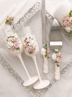 three white vases with pink and white flowers sit on a tray next to silverware