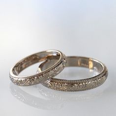 two wedding rings sitting next to each other on a white surface with reflections in the background