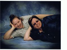 two women are laying on the ground posing for a photo with their arms around each other