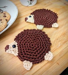 two crocheted coasters sitting on top of a wooden table next to cookies