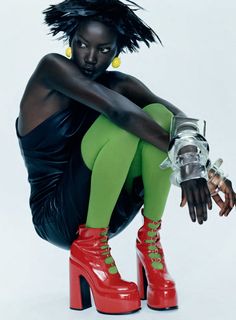 a woman in green tights and red high heeled shoes sitting on the ground