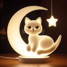 a white cat sitting on top of a table next to a moon and star light