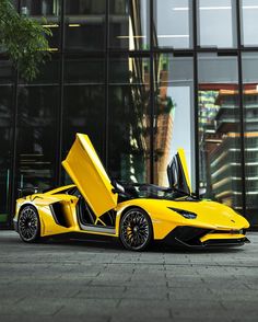 a yellow sports car parked in front of a tall building with its doors open and it's door opened