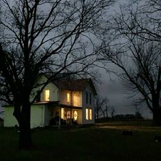 a white house sitting in the middle of a field at night with lights shining on it's windows