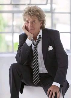 a man in a suit and tie sitting on a chair with his hand under his chin