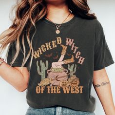 Stir up some Halloween fun with our "Wicked Witch of the West" T-shirt! This enchanting design features a bubbling cauldron with legs in cowgirl boots sticking out, surrounded by whimsical decorations like cacti, a broomstick, and jack-o-lanterns. Perfect for adding a touch of spooky Western charm to your fall wardrobe, this shirt is ideal for Halloween parties, casual outings, or cozying up with a spellbook. Made from soft, high-quality fabric, it ensures comfort and style as you embrace your w Witchy Halloween T-shirt With Graphic Print, Fall Novelty T-shirt With Funny Print, Funny Print Novelty T-shirt For Fall, Fall Witchy Graphic Print T-shirt, Witchy Short Sleeve T-shirt With Graphic Print, Witchy Halloween Crew Neck T-shirt, Witchy Crew Neck Halloween Tops, Witchy Crew Neck Top For Halloween, Witchy Short Sleeve Cotton Tops