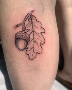 an oak leaf and acorn tattoo on the thigh, with two acorns