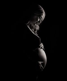 a pregnant woman standing in the dark with her hands on her belly and looking down