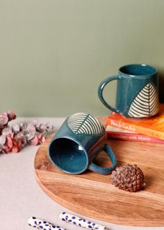 two coffee mugs sitting on top of a wooden tray next to books and pencils