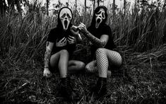 two people wearing masks sitting on the ground in front of some tall grass and plants