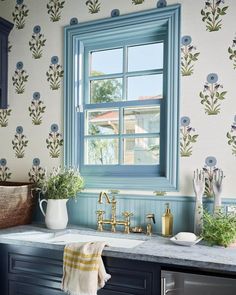 a kitchen with blue cabinets and wallpaper has a window above the sink that is decorated with flowers