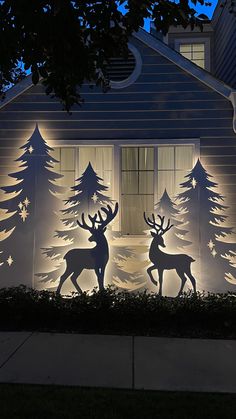 lighted christmas decorations in front of a house with trees and deers on the side