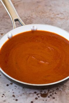 a white bowl filled with red sauce on top of a marble counter next to a silver spoon