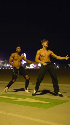 two shirtless men standing on top of an airport tarmac with their hands in the air