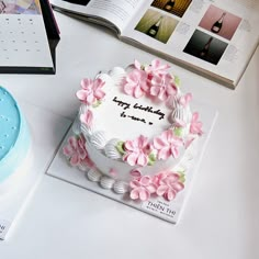 a birthday cake with pink flowers on it and an open book next to the cake