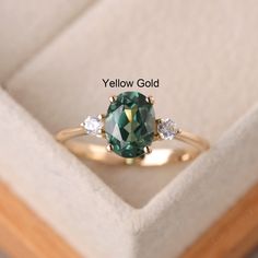 a green ring with three white diamonds in it's presentation box for the yellow gold