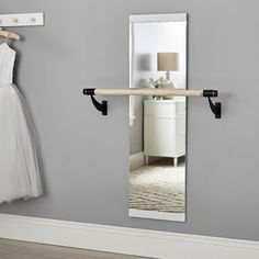 a white dress hanging on a rail next to a mirror and coat rack in a room