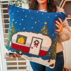 a woman holding up a crocheted pillow with a camper on the front