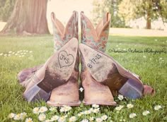 two cowboy boots with hearts on them sitting in the grass next to daisies and a tree