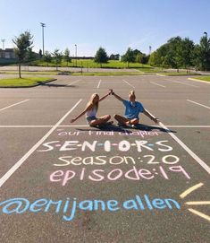 two people sitting in the middle of an empty parking lot with chalk writing on it