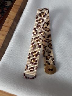 a beaded bracelet with a gold button on it sitting on a piece of cloth