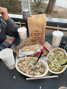 two plates of food sitting on top of a table next to coffee cups and paper napkins