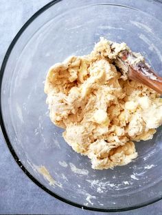 a glass bowl filled with food and a wooden spoon in it's center, on top of a gray surface