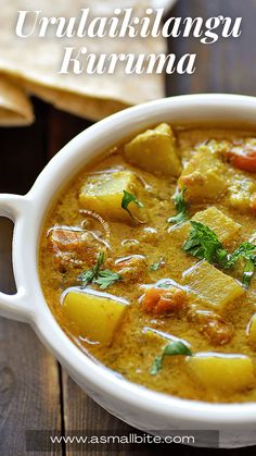 a white bowl filled with curry next to tortilla chips on a wooden table