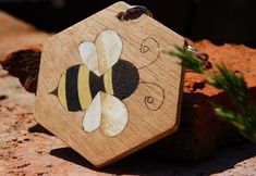 a wooden keychain with a bee painted on it's side sitting on some rocks