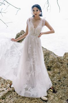 a woman standing on top of a rock near the ocean wearing a white wedding dress