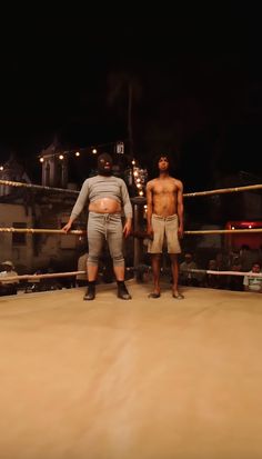 two men standing next to each other in front of a wrestling ring with ropes on the ground