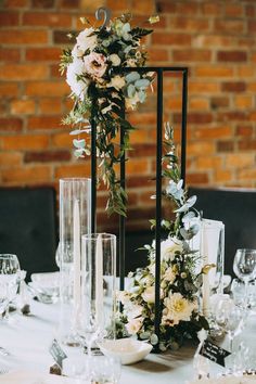 an arrangement of flowers and greenery on a table with candles, plates and glasses