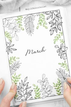 two hands holding a notebook with the word march written on it and surrounded by leaves