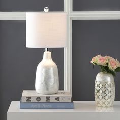 a white table lamp sitting on top of a book next to a vase with flowers