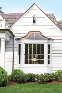 a white house with an arched window and green grass in the front yard, surrounded by shrubs