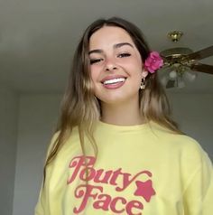 a woman with long hair wearing a yellow shirt and pink flower in her hair