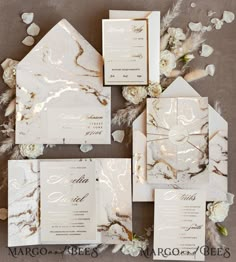 the wedding stationery is laid out on top of each other with white flowers and greenery