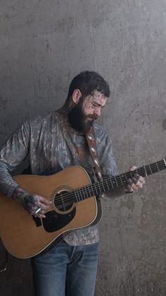 a man with makeup on his face and beard playing an acoustic guitar in front of a concrete wall