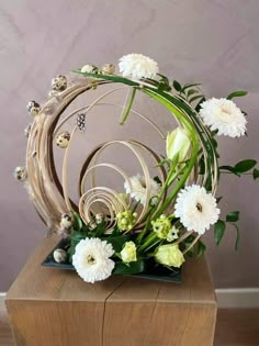 an arrangement of flowers is displayed on a wooden stand in front of a gray wall