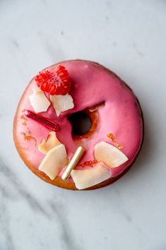 a pink donut with white icing and fruit toppings on it's top