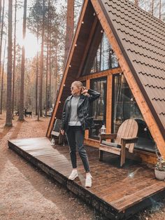 a woman standing on the porch of a small cabin in the woods with her feet up