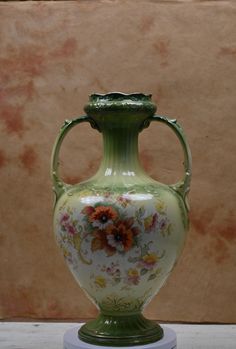 a green vase sitting on top of a white table next to a brown and tan wall