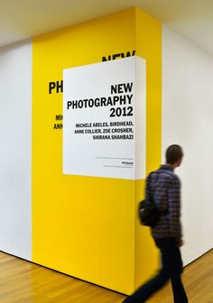 a man walking past a yellow and white wall next to a wooden floor in an art gallery